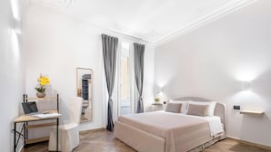 Quarto de hotel com cama, escrivaninha com laptop, cadeira, espelho e janela com cortinas.