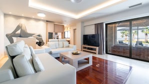 Ein modernes Wohnzimmer mit einem weißen Sofa, einem Couchtisch und einem Fernseher. Ein großes Fenster bietet Blick auf Palmen.