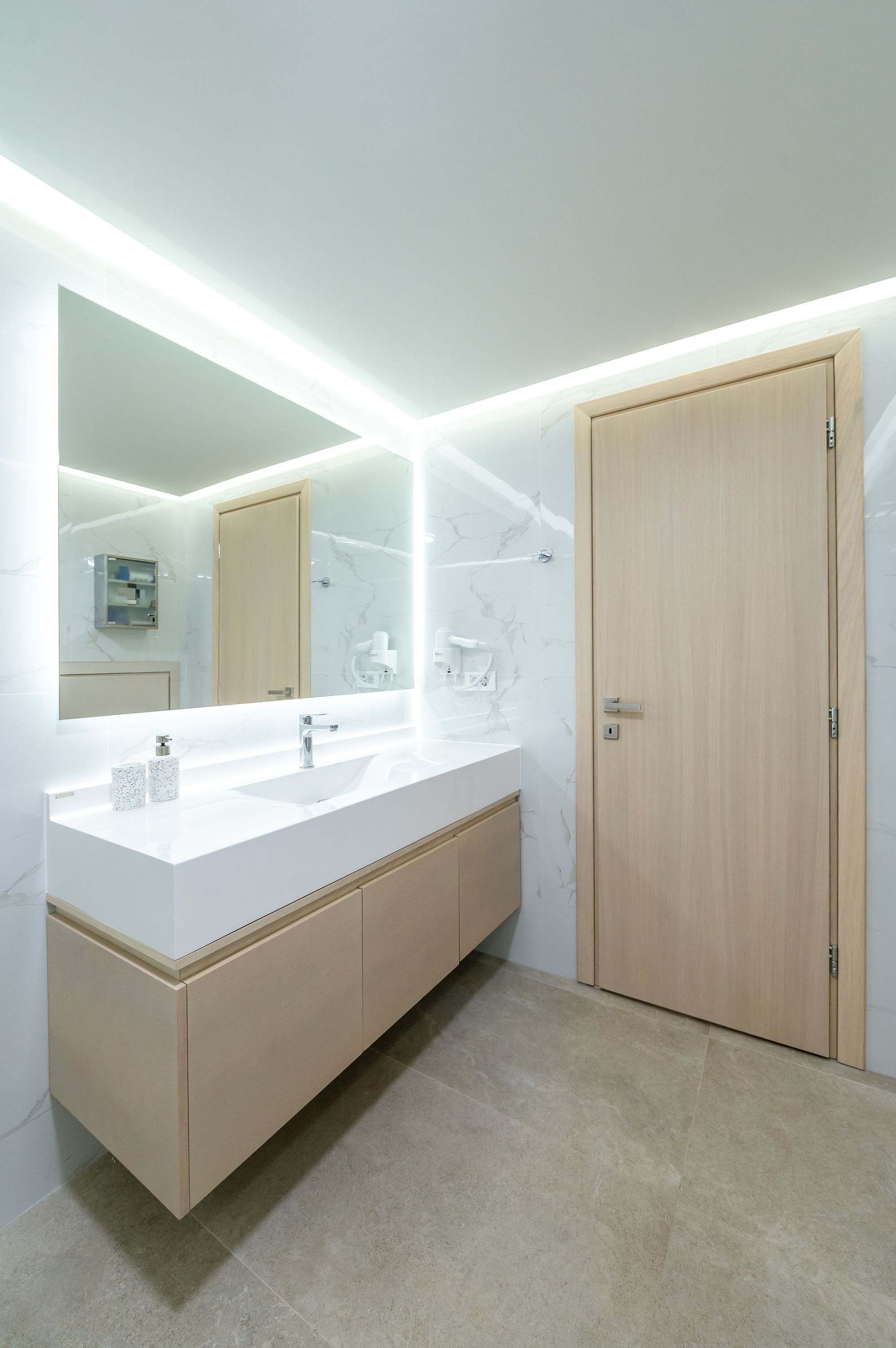 A modern bathroom with a large mirror, a white sink, and wooden cabinets.