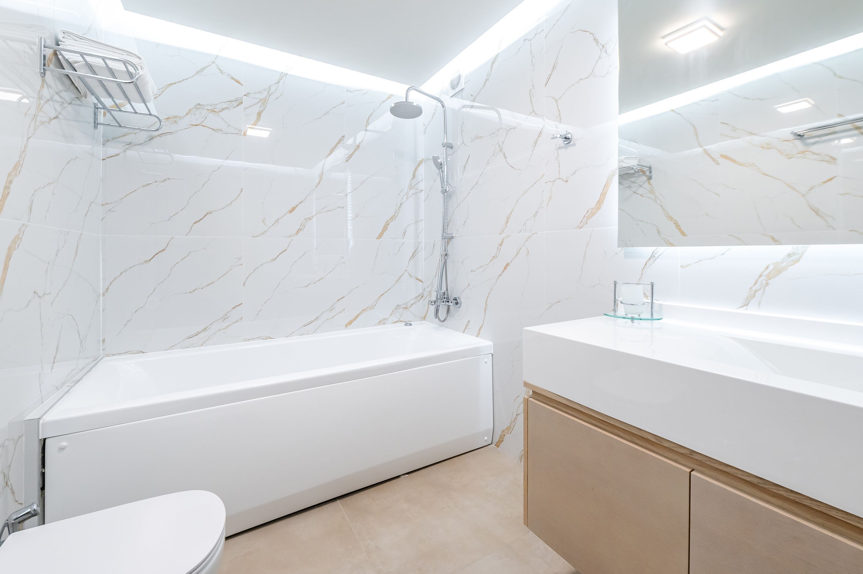 A modern bathroom with a white bathtub, a glass shower enclosure, and a marble-tiled wall.