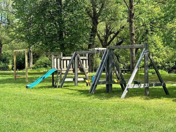 A playground with swings and a slide in a grassy park area.