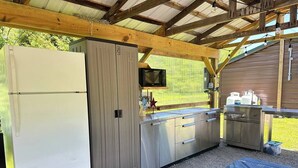 A covered outdoor kitchen area with a refrigerator, microwave, and stainless steel cabinets.