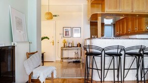 A modern kitchen with wooden cabinets, a bar area with stools, a dining table with chairs, and a television on a stand. - Cozy in Athens Neos Kosmos, an original vibe (Athina)