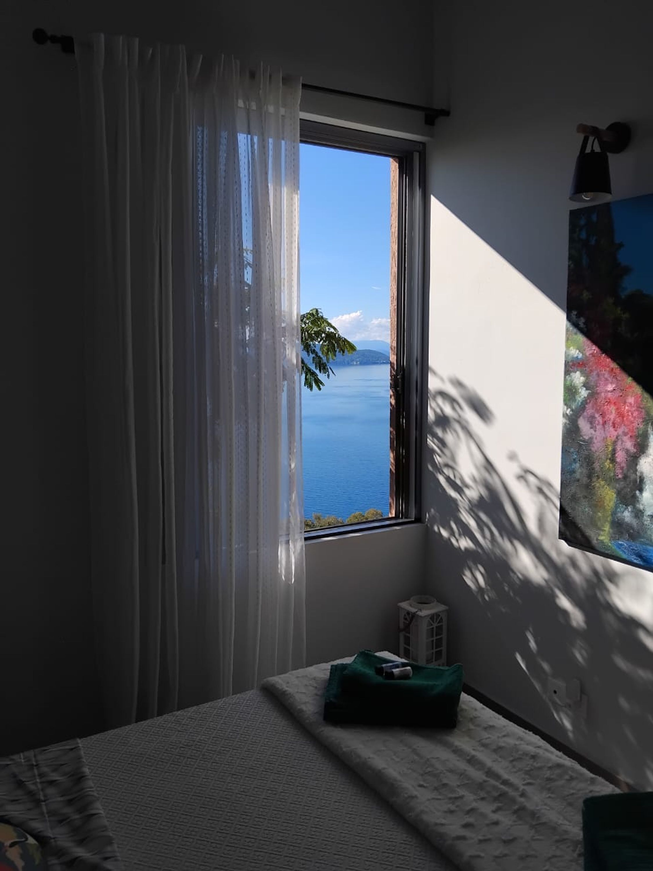 A bedroom with a window overlooking a body of water, a bed with a green pillow, and a wall-mounted air conditioner.
