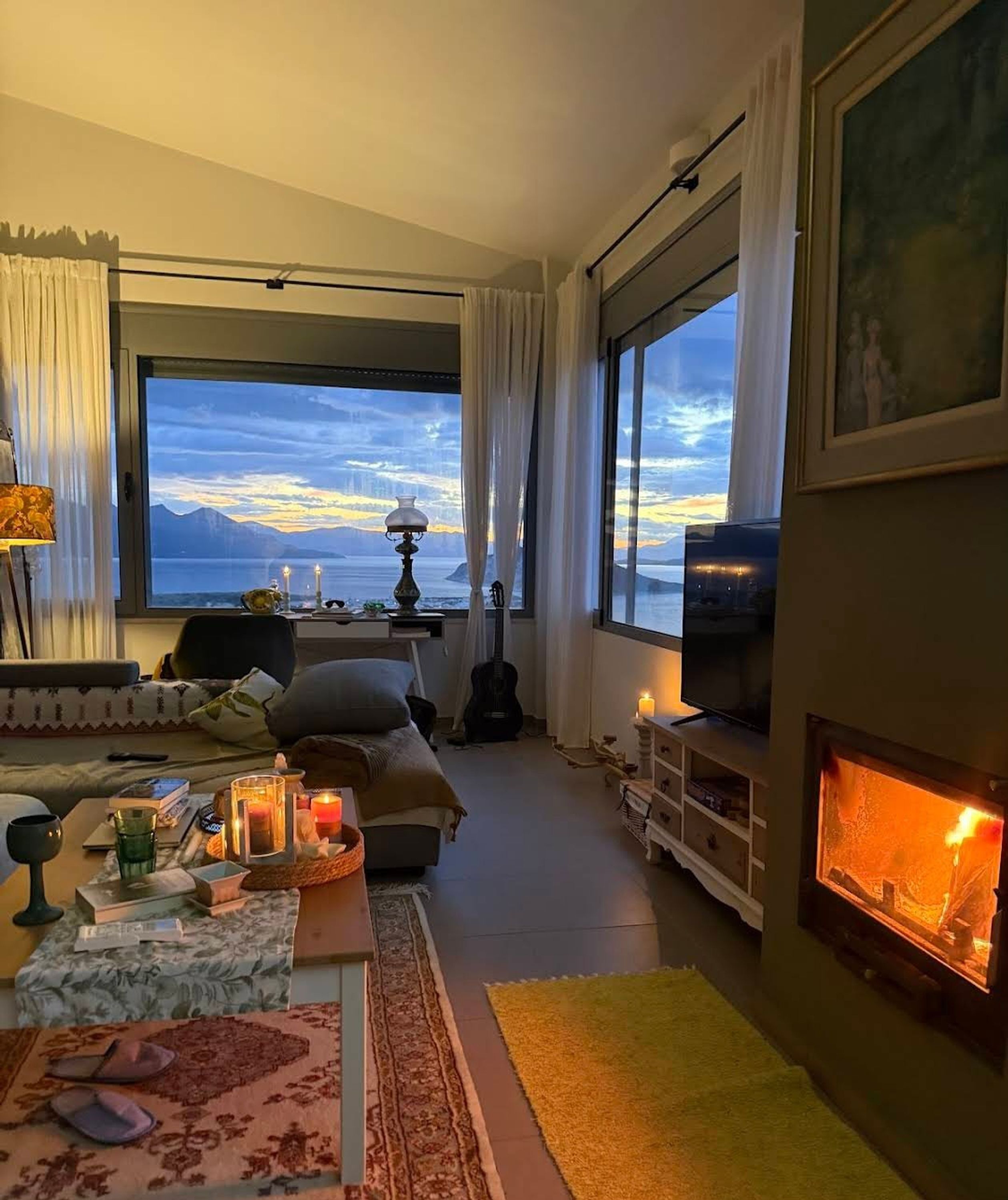 A cozy living room with a large window, a fireplace, and a view of the mountains.