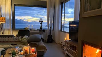 A cozy living room with a large window, a fireplace, and a view of the mountains.