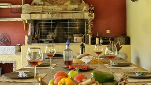 Una mesa de comedor dispuesta con copas de vino, una cesta de verduras y una rústica chimenea de piedra.