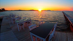 Terraza de madera con mesas y sillas mirando una puesta de sol sobre el agua.