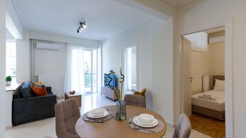 A modern living room with a dining table set for two, a sofa, and a TV in the background.