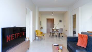 A modern living room with a flat-screen TV, a sofa, a coffee table, and a dining area with chairs and a table.