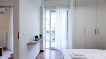 A bedroom with a bed, a wardrobe, a radiator, a shelf with a plant, and a view of the outside.