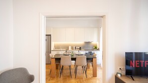 Une cuisine moderne avec des meubles blancs, une table à manger avec des chaises et un téléviseur affichant le logo de Netflix.