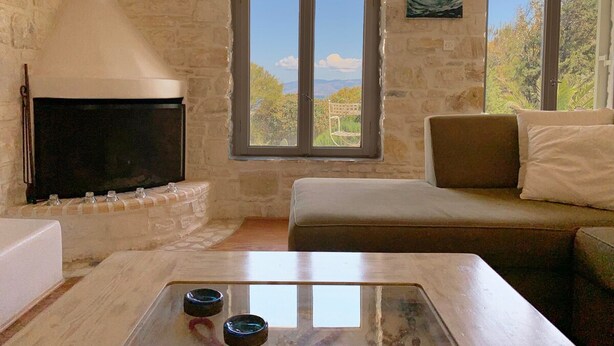 A stone-walled room with a fireplace, a sofa, and a table with glasses. - Villa Joy in Ampelas, Paros (Ampelas)
