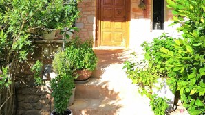 A stone building with a wooden door and a covered porch. There are potted plants around the entrance. - Villa Joy in Ampelas, Paros (Ampelas)