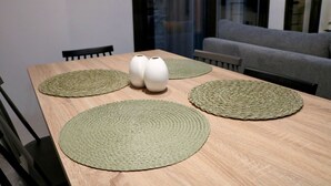 A dining table with four woven placemats, two white vases, and a grey sofa in the background. - No 2 - Theo Apartment two bedrooms ground floor (Athina)