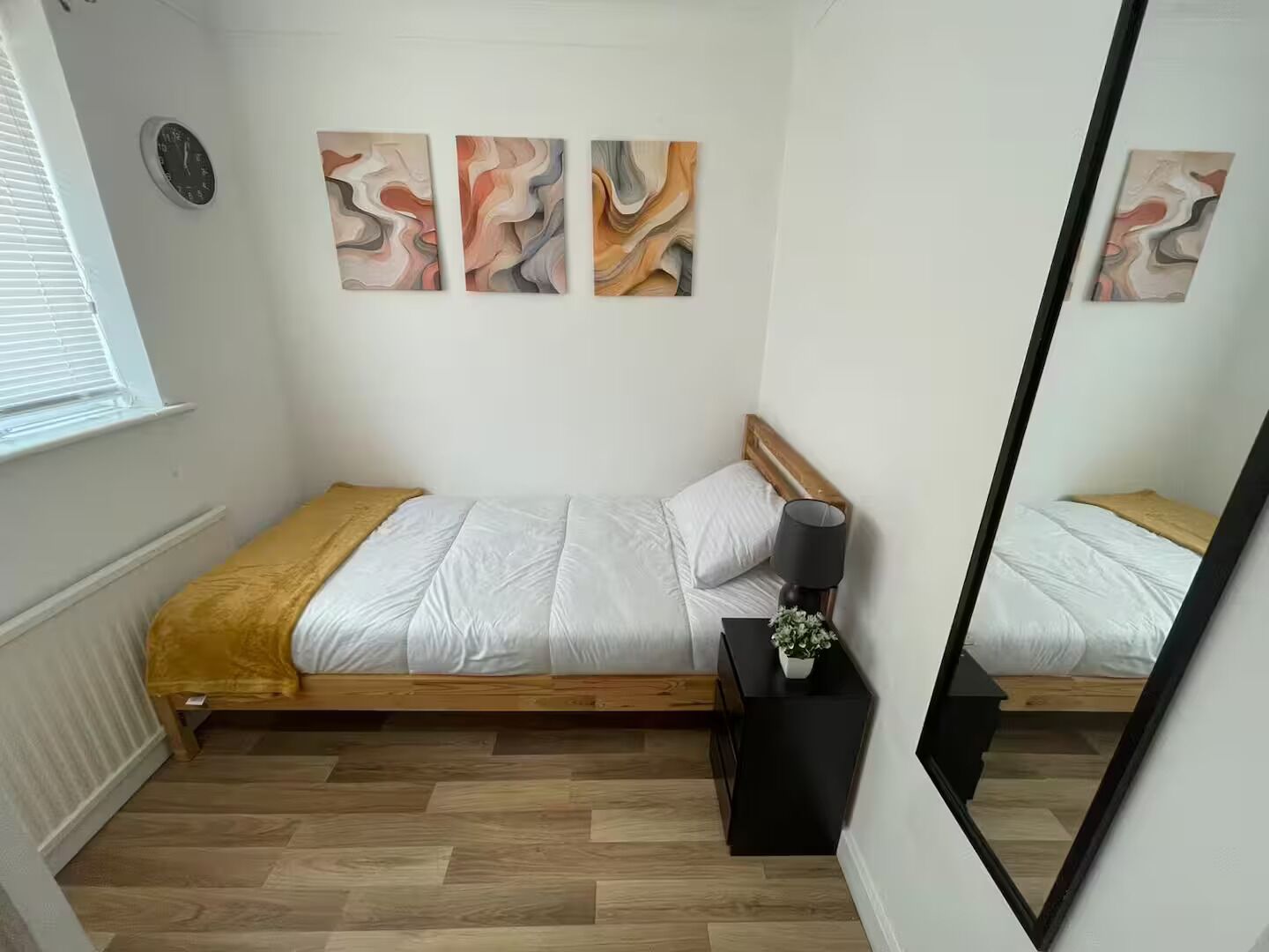 Une chambre à coucher avec un lit en bois, une table de chevet avec une lampe, et trois tableaux abstraits accrochés au mur.