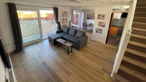 Un salon spacieux avec un canapé d’angle gris, une petite table et une porte-fenêtre coulissante donnant sur un jardin.