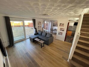 A spacious living room with a grey sectional sofa, a small table, and a sliding glass door leading to a backyard. - Tranquil 3-bedroom apartment with AC in pleasant Colchester (Colchester)