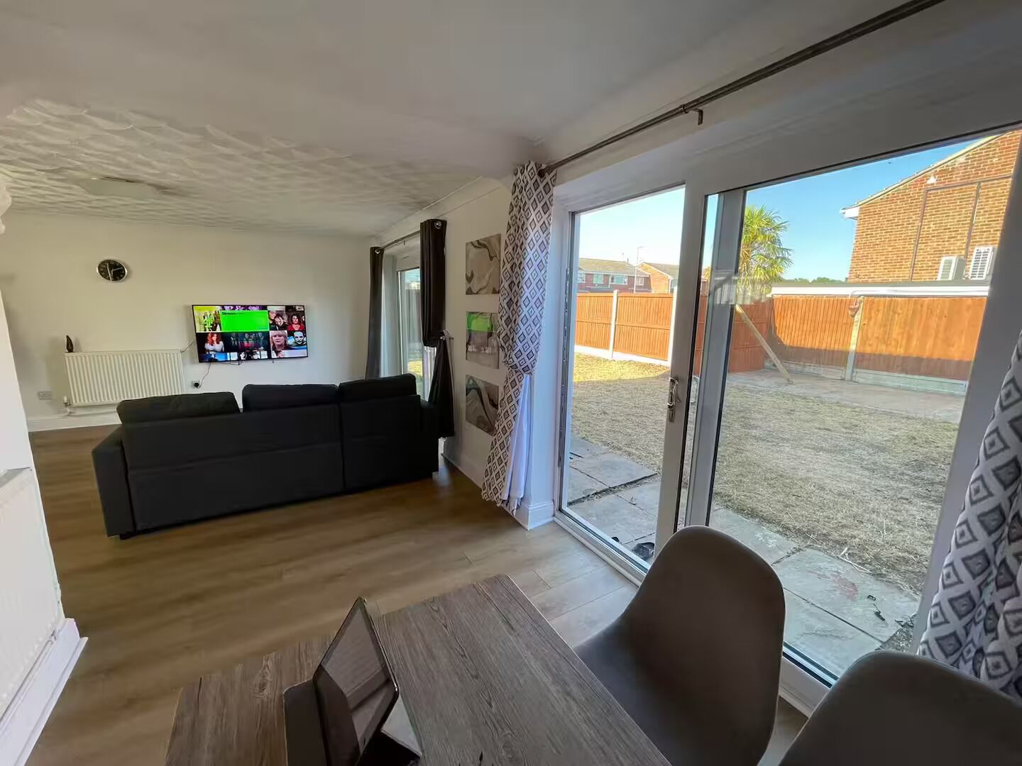 A living room with a black sofa, a TV mounted on the wall, and a sliding glass door leading to a backyard.