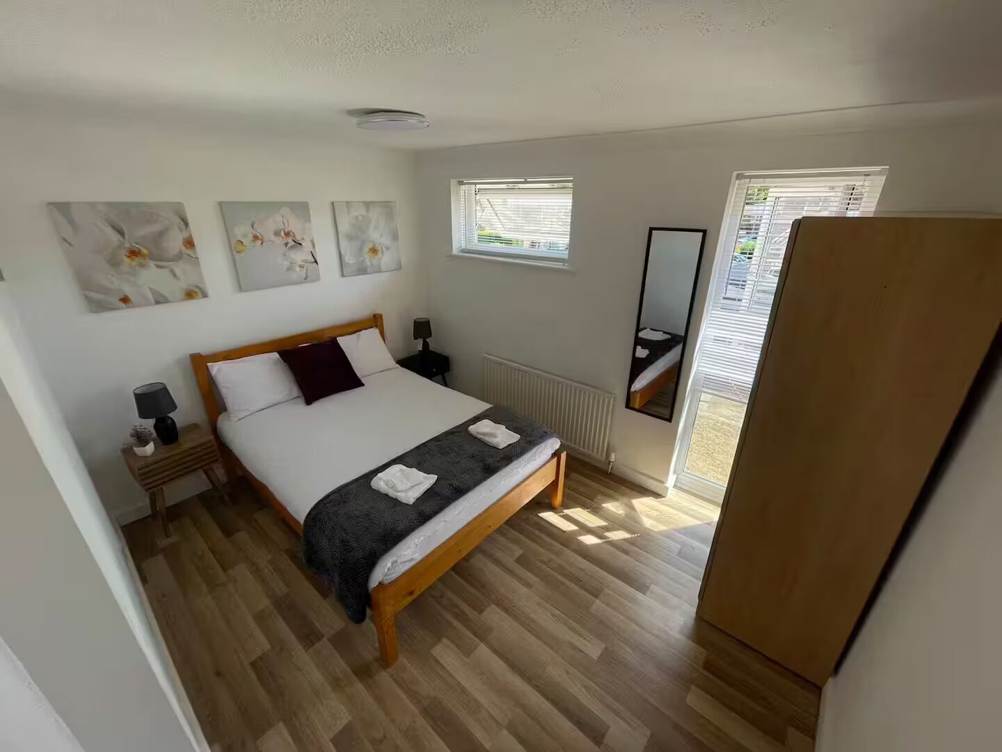 A bedroom with a wooden bed, a nightstand, a mirror, and artwork on the wall.