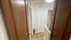 Un couloir étroit, avec des portes en bois et un parquet disposé en motif chevrons.