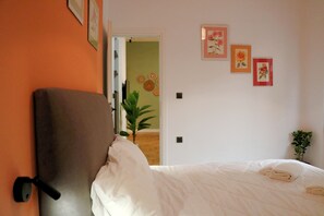 Ein Schlafzimmer mit einem Bett, einem Nachttisch, einer Topfpflanze und einer Tür zu einem anderen Raum.