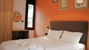 Un letto rifatto con lenzuola e asciugamani bianchi, uno specchio rotondo a parete e due quadri floreali incorniciati sopra il letto.