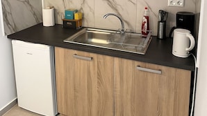 Eine kompakte Küche mit integriertem Spülbecken, Holzschränken, einem weißen Geschirrspüler und einer Marmor-Spritzschutzwand.