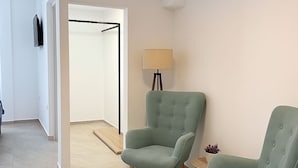 Ein modernes Zimmer mit zwei grünen Sesseln, einer Stehlampe und einem Kleiderständer im Hintergrund.