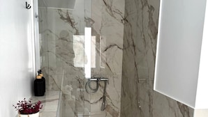 Ein modernes Badezimmer mit einer gläsernen Dusche, Marmorwänden und einem Blumentopf auf der Ablagefläche.