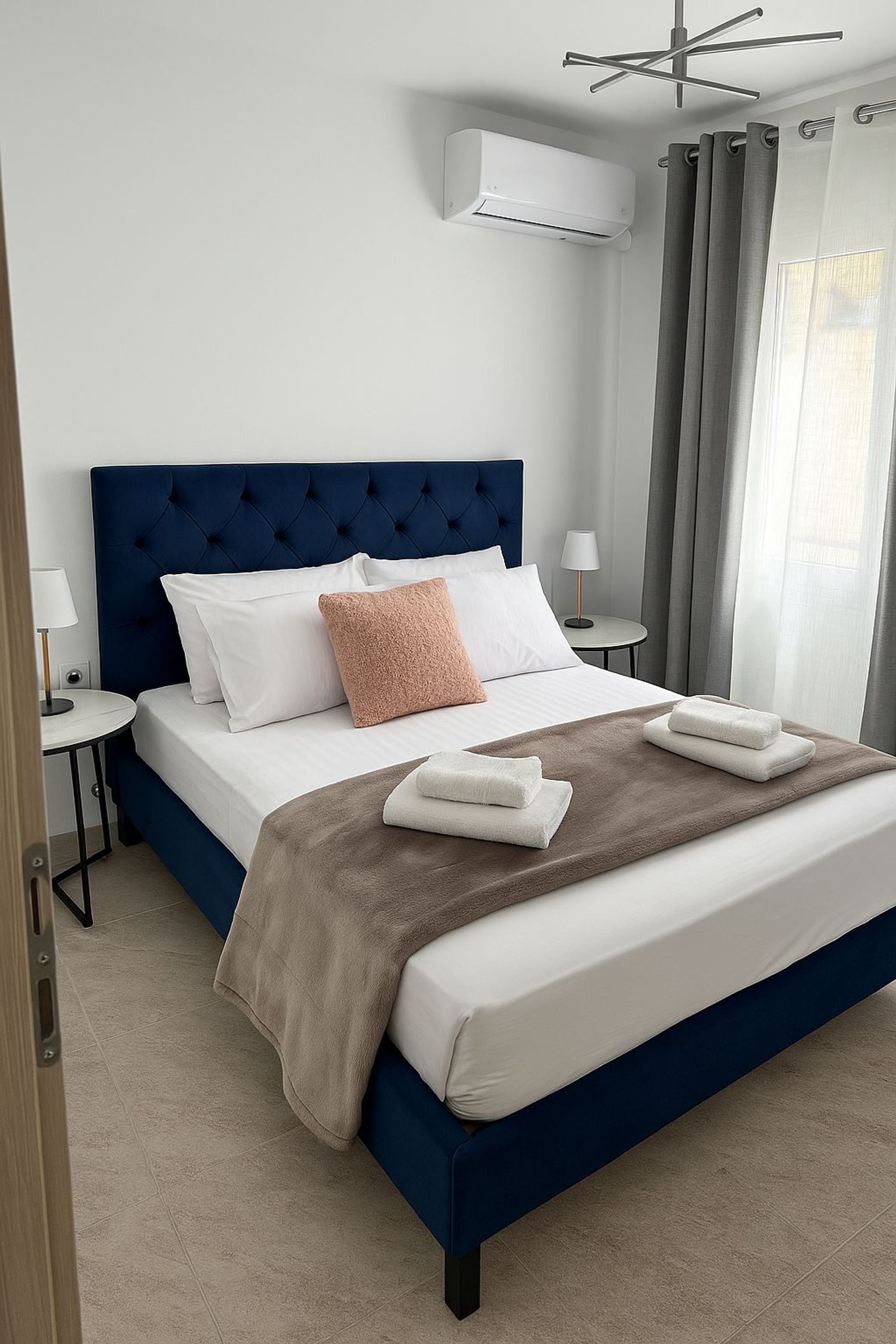 Ein modernes Hotelzimmer mit einem großen Bett, einem gepolsterten Kopfteil, weißer Bettwäsche, einer braunen Tagesdecke und einem kleinen Nachttisch mit Lampe.