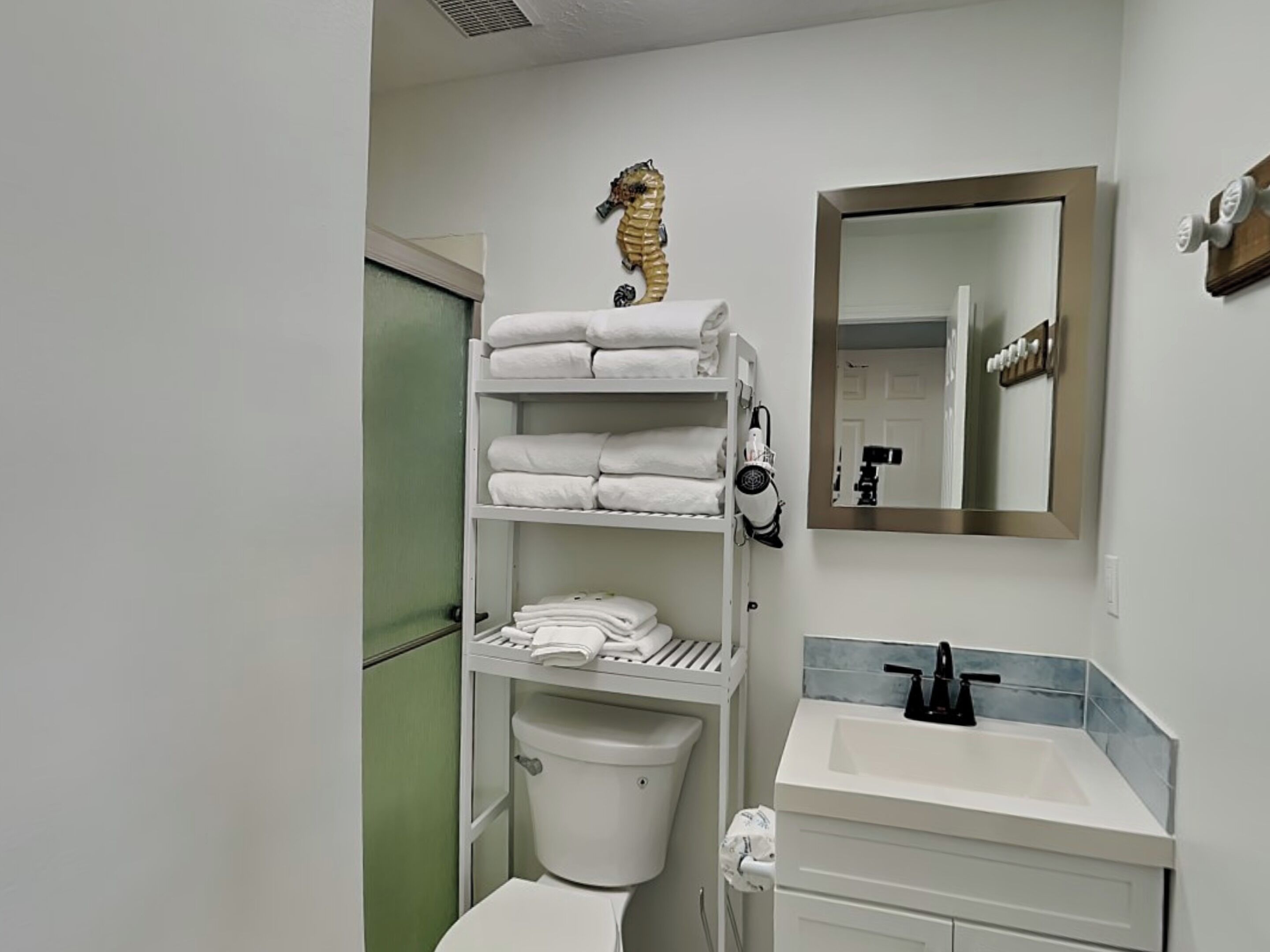 A bathroom with a toilet, a sink, a mirror, and a shelf with towels.