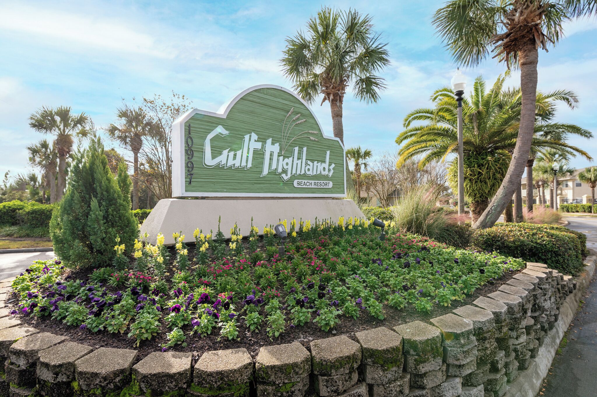A sign for Gulf Highlands Beach Resort surrounded by a landscaped garden with various plants and a stone wall.