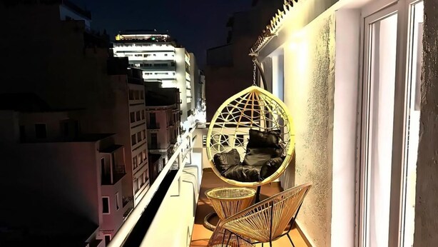 Een balkon met een rieten stoel en een hangstoel, een betegelde vloer en een leuning.