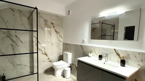 Een moderne badkamer met een marmeren spatwand, een toilet, een wastafel met spiegel erboven en een douchegedeelte.