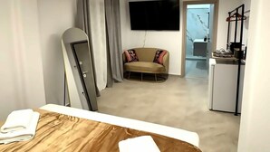Een moderne hotelkamer met een bed, een sofa, een televisie en een kitchenette.