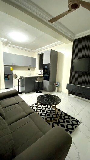 A modern living room with a sofa, a black and white patterned rug, a small round table, and a kitchen area with cabinets and appliances. - Deluxe One Bed room Apartment, BH Apartments (Dansoman)