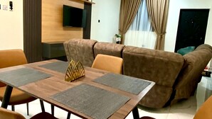 A modern living room with a dining area, a sofa, a TV, and a ceiling fan. - Two Bedroom Apartment, BH Apartments Dansoman Heights (Dansoman)