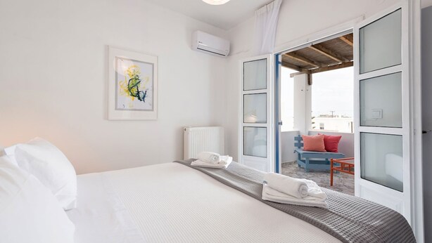 Ein Hotelzimmer mit Bett, Heizkörper, Klimaanlage, einem gerahmten Kunstwerk und Blick auf einen Außenbereich mit Sitzgelegenheiten.