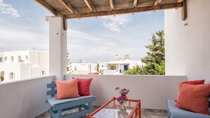Ein Balkon mit einer blauen Bank und einem Glastisch, mit Blick auf eine Küstenstadt mit weißen Gebäuden und blauem Himmel.