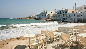 Un cadre idyllique en bord de mer, avec des bâtiments blancs, une plage de sable et les vagues de l’océan.