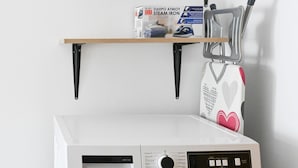 Een wasmachine met voorlader, voorzien van een bedieningspaneel, een klein plankje erboven en een witte handdoek aan een rek.