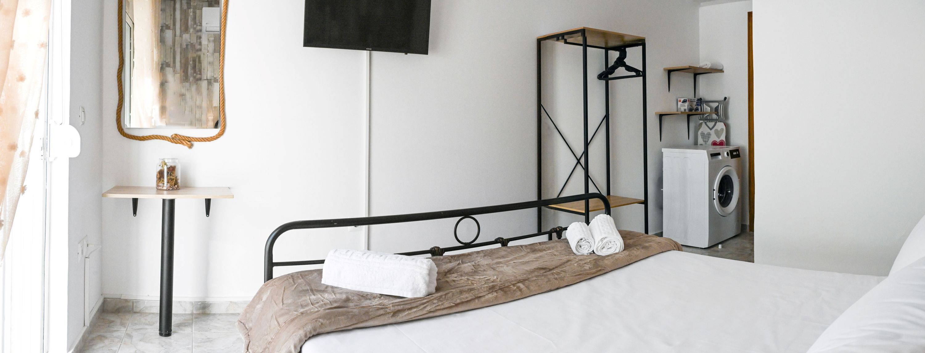 Ein Hotelzimmer mit Bett, einer Waschmaschine, einem Spiegel, einem Ablagebereich mit Pflegeprodukten und einem Fenster mit Vorhängen.