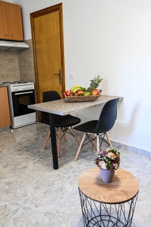 Una cocina con encimera de granito, dos sillas negras, una mesa de madera, una planta en maceta y una cesta de fruta.