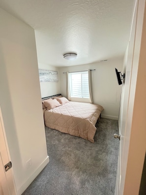 A bedroom with a bed, a window with curtains, a ceiling light, and a door.