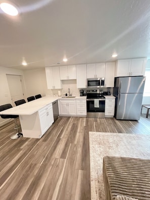 A modern kitchen with white cabinets, stainless steel appliances, and a wooden floor.