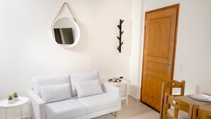 Un canapé blanc, un miroir rond, une porte en bois, une petite table avec un plateau, et une chaise en bois.