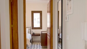 Un couloir menant à une chambre à coucher équipée d’un lit, d’une table de chevet et d’une fenêtre.