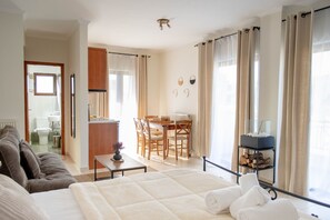Habitación de hotel con cama, sofá, zona de comedor con sillas, una pequeña mesa y vistas a la ciudad.