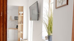 Un corridoio con pavimento in legno, un tavolino con tovaglia decorata, una pianta in vaso e un quadro appeso al muro.